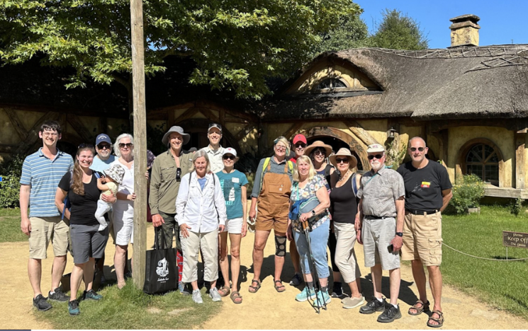 Group os adults stands in front of a thatched cottage in Hobbiton